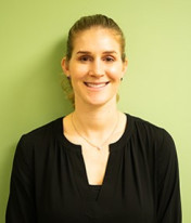 a white woman with brown hair and wearing a black shirt stands smiling in front of a green wall